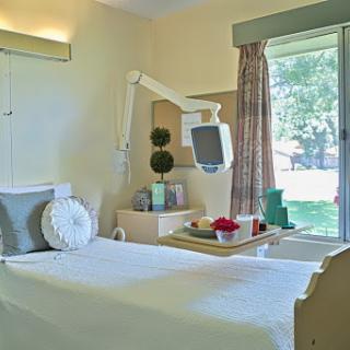 A well-lit hospital room featuring a bed, medical equipment, and a view of the outdoors.
