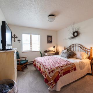 A cozy bedroom with a neatly made bed, television, and various decorative elements.