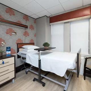 A clean and organized hospital room featuring a bed, nightstand, and chair.