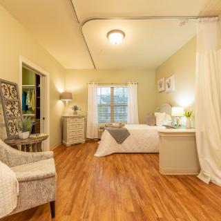 A cozy bedroom with wooden flooring, featuring a comfortable bed, a stylish chair, and soft lighting.