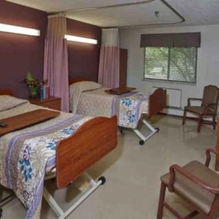 A hospital room with two patient beds, chairs, and a window.
