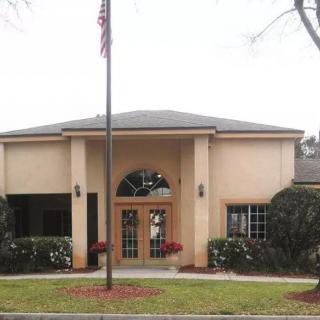 A beige building with a central entrance, surrounded by plants and featuring an American flag at the front.