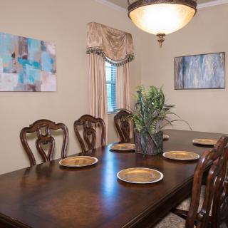 A classic dining room setup with a wooden table and chairs, decorated with plates, artwork on the walls, and illuminated by a chandelier.