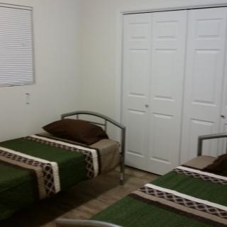 A minimalist bedroom with twin beds featuring green bedding and a closet.