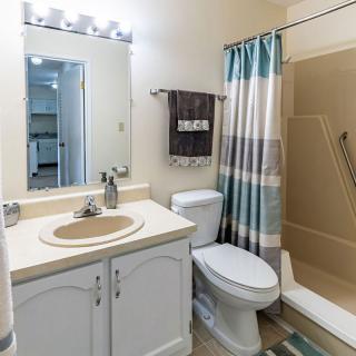 A clean and modern bathroom with a sink, mirror, toilet, and shower area.