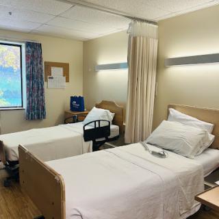 A view of a hospital patient room with two beds and natural light coming through the window.