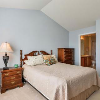 A cozy bedroom with a classic wooden bed, matching nightstand, and dresser. The room features soft blue walls and a lamp providing warm lighting.