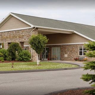 A modern building with a stone facade and landscaped surroundings, featuring a circular driveway leading to the entrance.