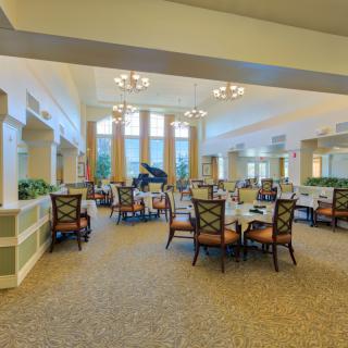 A spacious dining area with elegant furniture, featuring a grand piano and large windows.