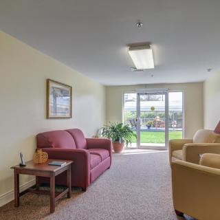 A cozy living room with a red sofa, beige chairs, and a large window overlooking a garden.