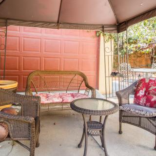 A cozy outdoor patio setup under a gazebo with wicker chairs, a swing bench, and a small round table.