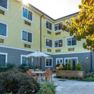 A residential building with a sunny courtyard featuring outdoor seating and greenery.