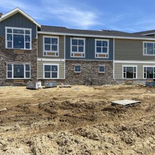 A newly constructed building with a mix of stone and siding exterior, surrounded by an unfinished construction site.