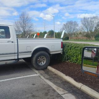 A white truck parked awkwardly, partially on the bushes.