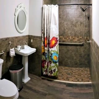 A modern bathroom featuring a tiled walk-in shower with a colorful curtain, pedestal sink, and toilet.