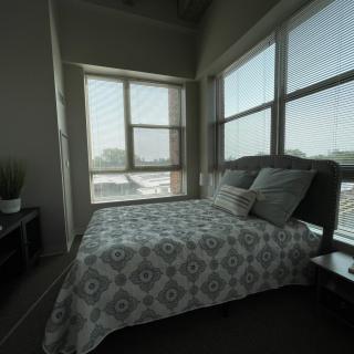 A cozy bedroom with a large bed, patterned bedding, and ample natural light from surrounding windows.