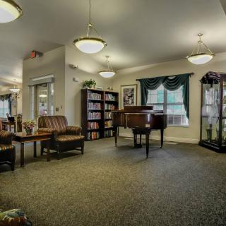 A cozy lobby area featuring comfortable seating, a piano, bookshelves, and large windows.