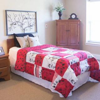 A cozy bedroom featuring a bed with a colorful quilt and wooden furniture.
