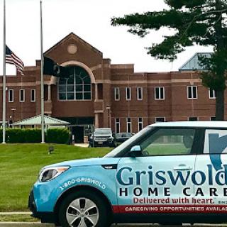 A Griswold Home Care vehicle parked in front of a building with flags.