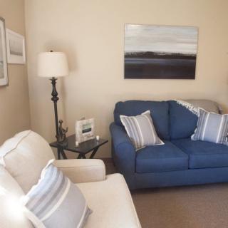 A cozy living room with a blue sofa and striped cushions, decorated with wall art and a lamp.