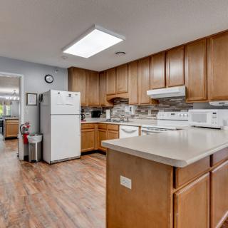 A spacious kitchen with wooden cabinets and white appliances, including a refrigerator and stovetop, featuring a hardwood floor.