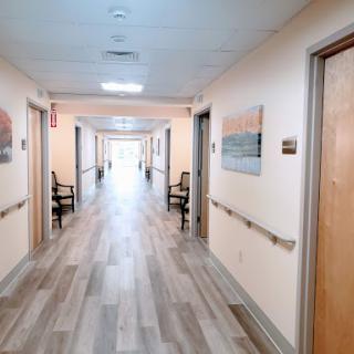 A serene hospital hallway featuring wooden doors, seating areas, and artwork on the walls.