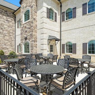 A spacious outdoor patio area with several tables and chairs, adjacent to a brick building with large windows.