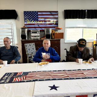 A group of veterans enjoying a meal together in a community space decorated with an American flag.