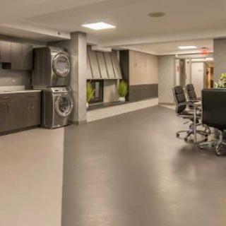 A modern multi-purpose space featuring a laundry area with stackable washers and dryers, alongside an office-style meeting area with chairs.