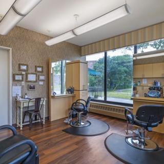 An empty hair salon with chairs and mirrors, featuring large windows allowing natural light.