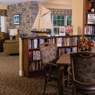 A cozy library corner with bookshelves, a table, and chairs, featuring a model ship and a window view.