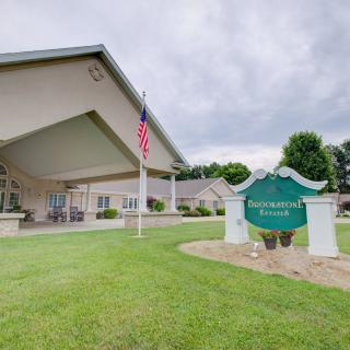 A building entrance with an American flag and a green sign on a well-maintained lawn under cloudy skies.
