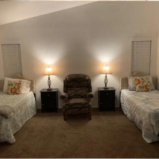 A cozy bedroom featuring twin beds with a central armchair, illuminated by two bedside lamps on nightstands.
