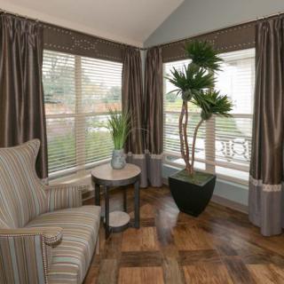 A cozy corner of a living room featuring a striped armchair, large potted plant, and windows with curtains.