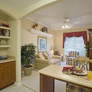 A cozy living room and dining area with traditional decor, featuring a sofa, armchair, and indoor plants.