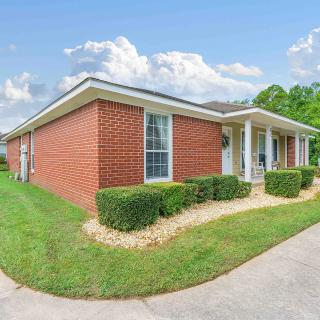 A single-story brick house with a well-maintained lawn and driveway under a partly cloudy sky.