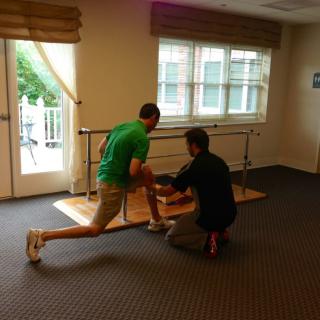 A physical therapy session with a person performing an exercise under the guidance of a therapist indoors.