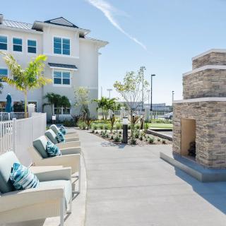 Outdoor seating area with chairs and a fireplace next to a modern building on a sunny day.