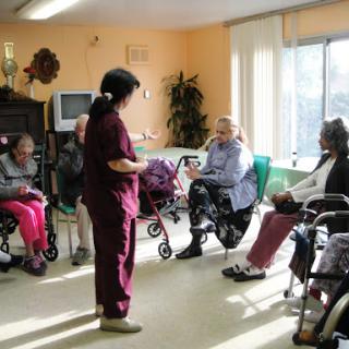 A caregiver engages with a group of elderly residents in a nursing home, fostering social interaction and community.