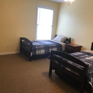A cozy bedroom featuring two beds, a nightstand, and natural light coming in from the window.