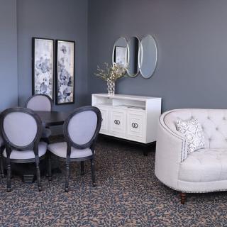 A stylish living room with a cozy white sofa, elegant dining chairs and table, complemented by wall mirrors and framed artwork.