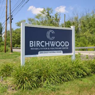 A sign for Birchwood, surrounded by greenery and under a clear blue sky.