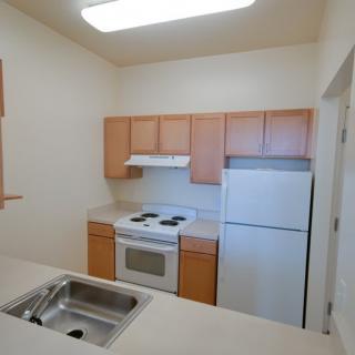 A small apartment kitchen with wooden cabinets, a stove, sink, and refrigerator.