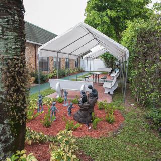 A well-maintained garden featuring a canopy-covered seating area, surrounded by decorative landscaping and sculptures.