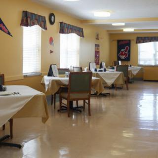 An empty dining room with tables and chairs set up, featuring yellow walls and bright lighting.
