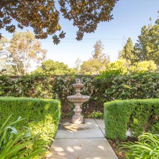 A serene garden pathway with a central fountain surrounded by lush greenery and hedges.