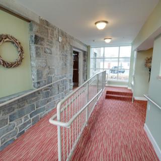 A carpeted hallway with a ramp and handrails, featuring a stone wall and decorative wreath.