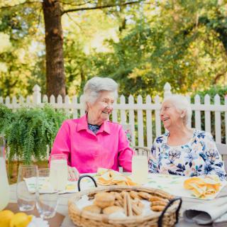 Two elderly women enjoying a conversation over snacks in a garden setting.