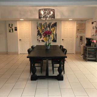 A modern dining room featuring a large wooden table with a decorative vase, surrounded by chairs and illuminated by a chandelier, with artwork adorning the walls.