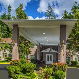 A grand entrance to a building surrounded by lush landscaping and tall trees under a blue sky with clouds.